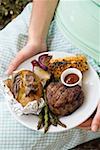 Woman holding a plate of grilled steak and accompaniments