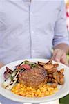 Man holding plate of grilled steak and accompaniments