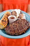 Woman holding plate of steak, corn on the cob, baked potato