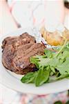 Woman holding plate of grilled steak, baked potato & salad