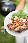 Woman holding plate of grilled chicken legs & pasta salad