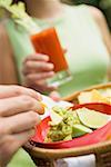 Hand hält Korb mit Guacamole & Chips, Frau mit Tomaten-Getränk