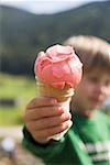 Small boy holding strawberry ice cream cone in outstretched hand