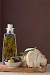 Thyme oil in bottle, olives & white bread on chopping board