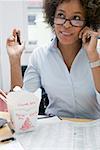 Femme dans le bureau avec le plat de nouilles asiatiques, sur le téléphone