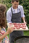 Man holding raw burgers over barbecue, woman holding iced tea