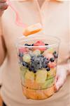 Woman taking piece of melon out of plastic tub of fruit salad