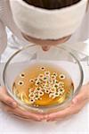 Woman bending over bowl of chamomile tea with flowers