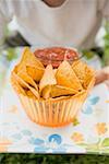 Child holding nachos and tomato salsa on tray