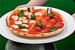 Hands holding tomato and mozzarella pizza with flags