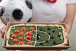 Female footballer holding spinach pizza with tomatoes & olives