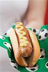 Femme tenant un hot dog à la moutarde sur la serviette avec des motifs de football