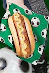 Hand mit Hot-Dog mit Senf auf Serviette mit Fußball-Motiven