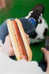 Football fan holding hot dog with mustard and remote