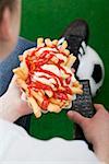 Football fan holding chips and remote