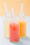 Three fruit juices in bottles with straws