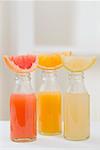 Three fruit juices in bottles with wedges of fresh fruit