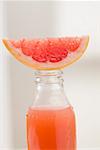 Pink grapefruit juice in bottle with fresh grapefruit wedge