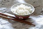 Rice in Asian bowl on newspaper, chopsticks beside it