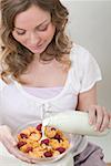 Woman pouring milk onto cornflakes with raspberries