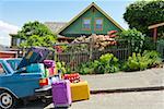 Car trunk loaded with colorful suitcases in front of house