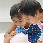 Close-up of two girls inserting coins into a piggy bank