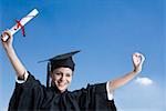 Portrait of a young female graduate holding a diploma with her arms raised and smiling