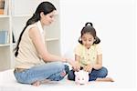 Mid adult woman and her daughter looking at a piggy bank