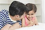 Close-up of a mid adult man with his daughter lying on the bed and smiling