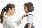 Profil de côté d'une jeune femme aide sa fille à porter l'uniforme scolaire et souriant