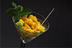 Close-up of a martini glass with mango slices and mint leaves