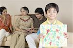 Portrait of a boy holding a painting and family sitting behind him