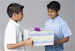 Side profile of a boy giving a gift to another boy and smiling