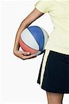 Mid section view of a teenage girl holding a basketball under the arm
