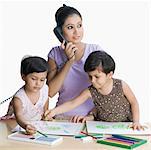 Two girls drawing in sketch pads and their mother talking on the telephone