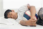 Boy sleeping on the bed and holding a football