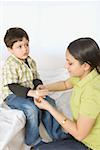 Close-up of a young woman applying a bandage to her son's hand