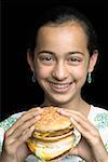 Portrait d'une jeune fille tenant un burger et souriant