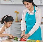 Mid adult woman with her daughter cutting vegetables on a cutting board in the kitchen