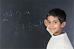 Portrait d'un garçon de résolution de symboles mathématiques sur un tableau noir