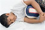 High angle view of a boy sleeping on the bed and holding a football