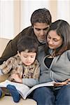 Boy sitting on a couch with his parents and looking at a picture book