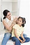 Mid adult woman combing hair of her daughter and smiling