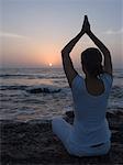 Rear view of a young woman meditating in a prayer position on the beach, Mud Island, Mumbai, Maharashtra, India