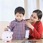 Boy putting a coin in a piggy bank with his mother sitting beside him