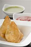 Close-up of two samosas with sauce