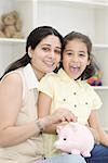 Portrait of a mid adult woman putting a coin in a piggy bank and smiling with her daughter