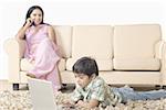 Boy using a laptop and mother talking on a mobile phone
