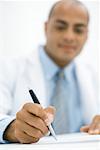 Doctor writing a prescription, focus on hand in the foreground