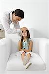Male doctor feeling young patient's forehead, girl sitting on armchair